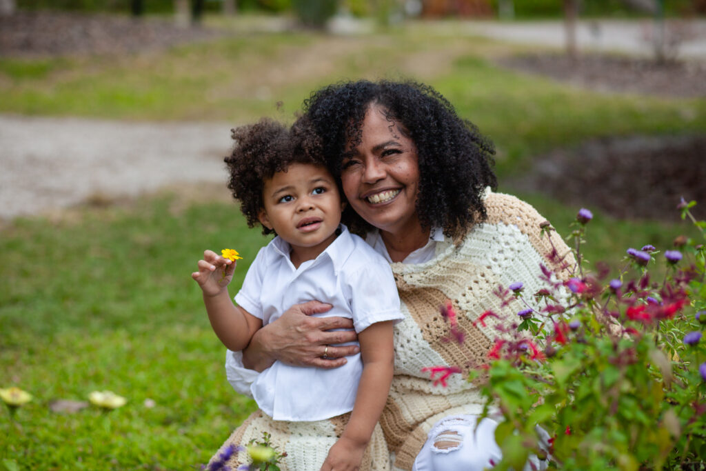 Grandma holds young grandson next to flower bed