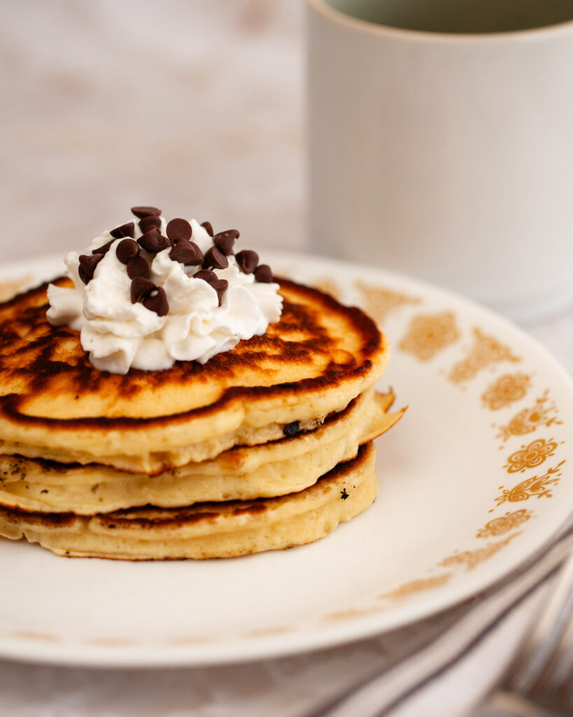 A stack of chocolate chip pancakes with whipped cream and chocolate chip toppings