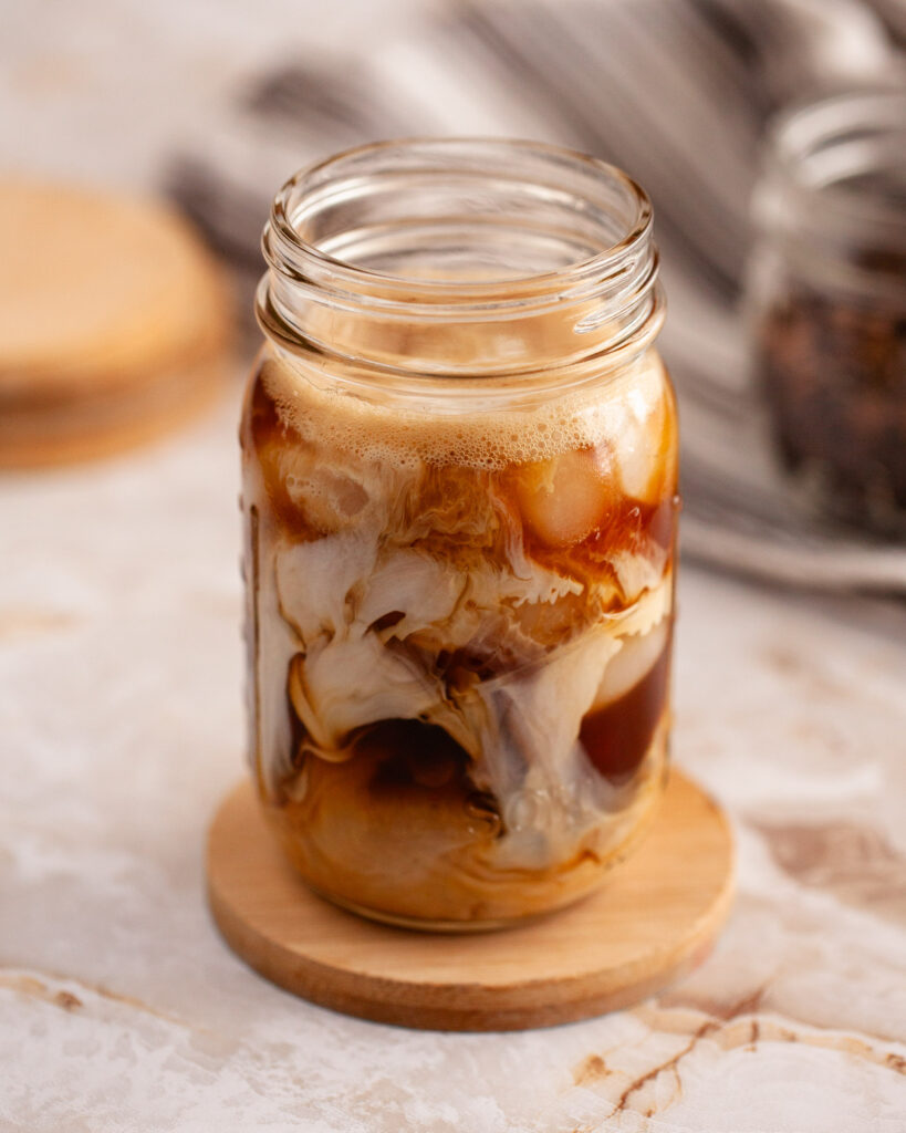 Cream swirling into iced coffee in a mason jar