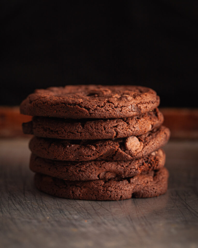 A stack of double chocolate chip cookies in a  dark and moody photography style