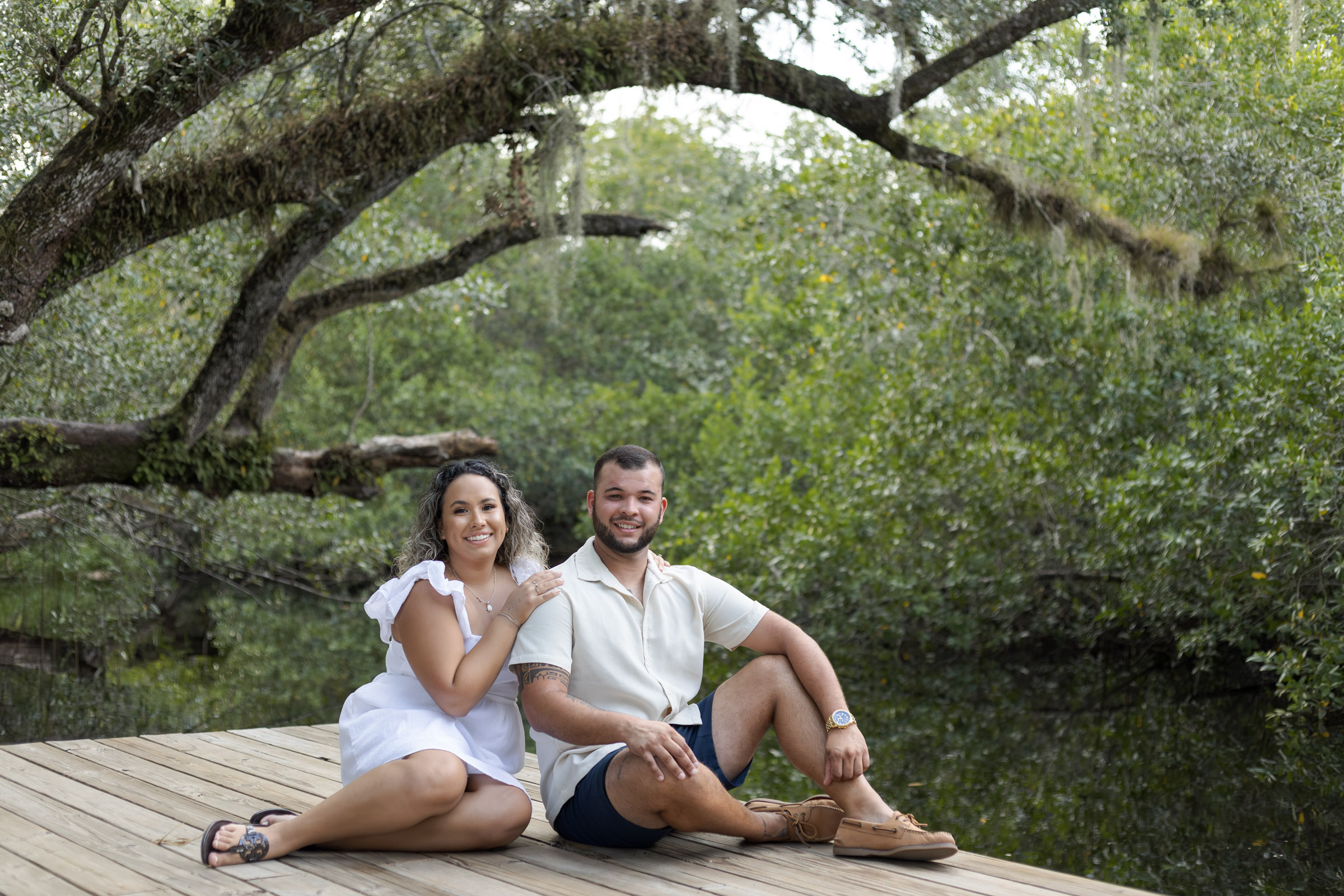 A couple sits on the dock at Koreshan State Park with an oak tree behind them