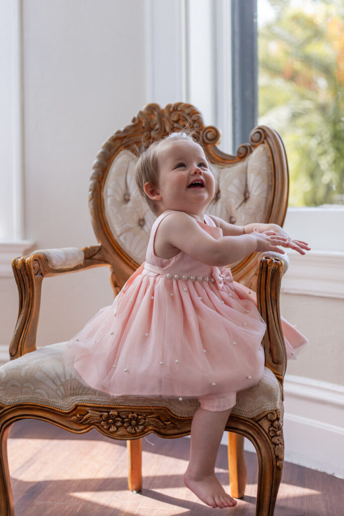 One year old girl laughing and sitting on vintage chair