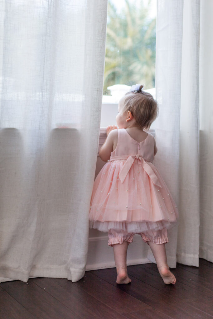 One year old in pink dress looks out the window