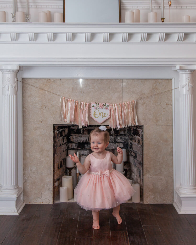 First birthday banner hangs on fireplace behind baby girl