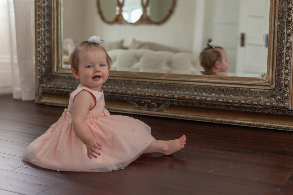 baby in pink dress in front of mirror