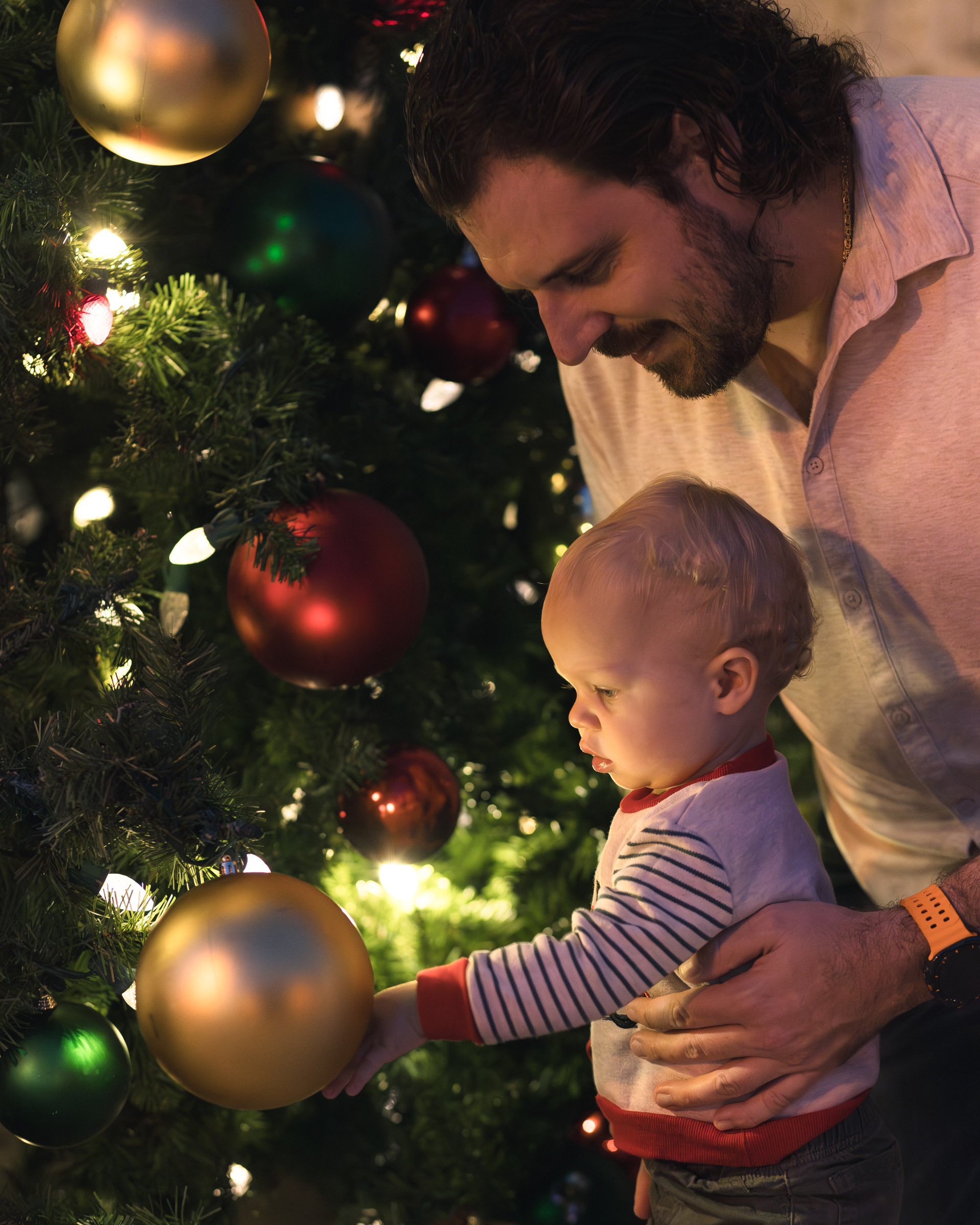 Father holds his son while he looks with wonder in his eyes at the large Christmas ornament