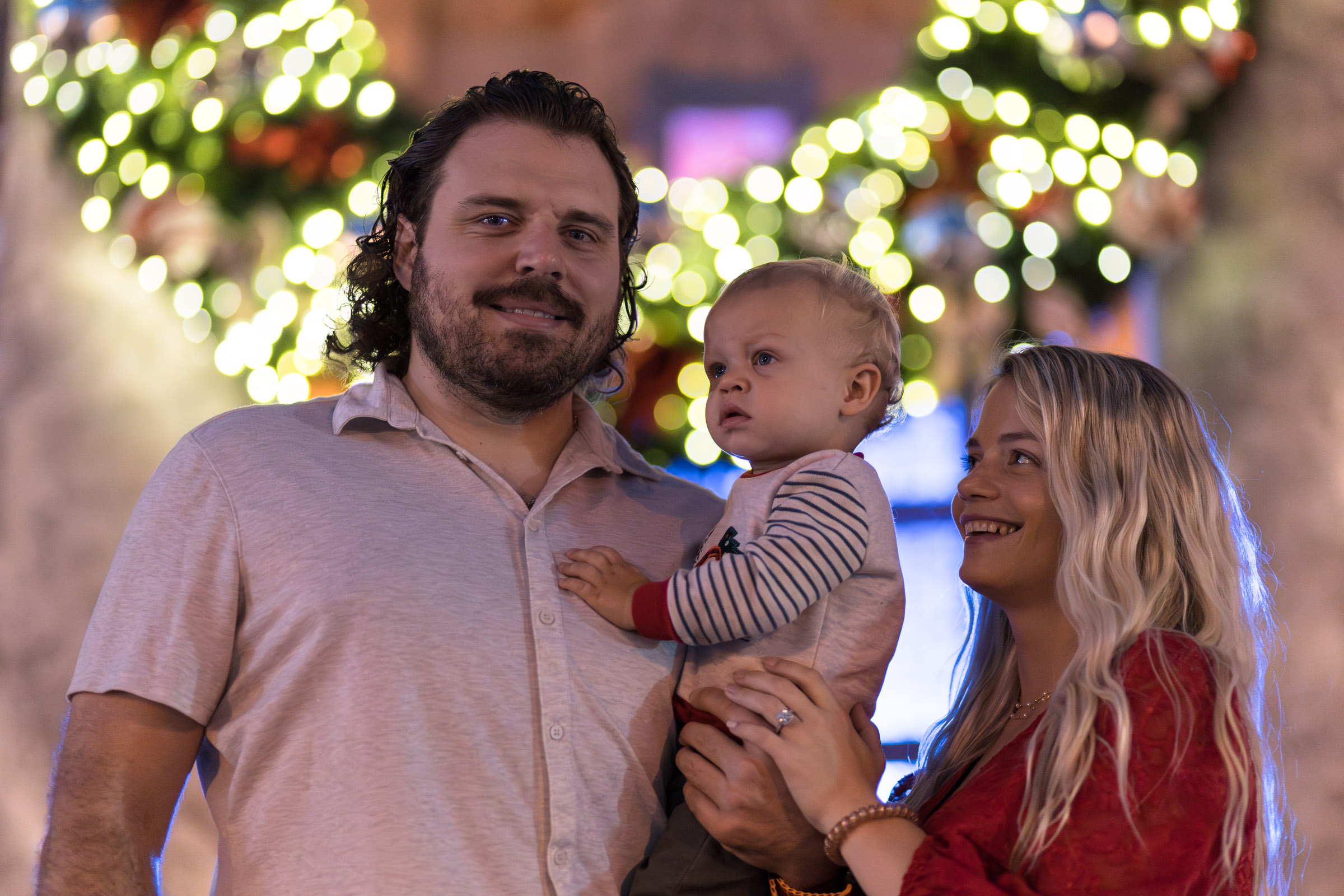 Family of 3 with a large Christmas wreath in the background in Downtown Fort Myers