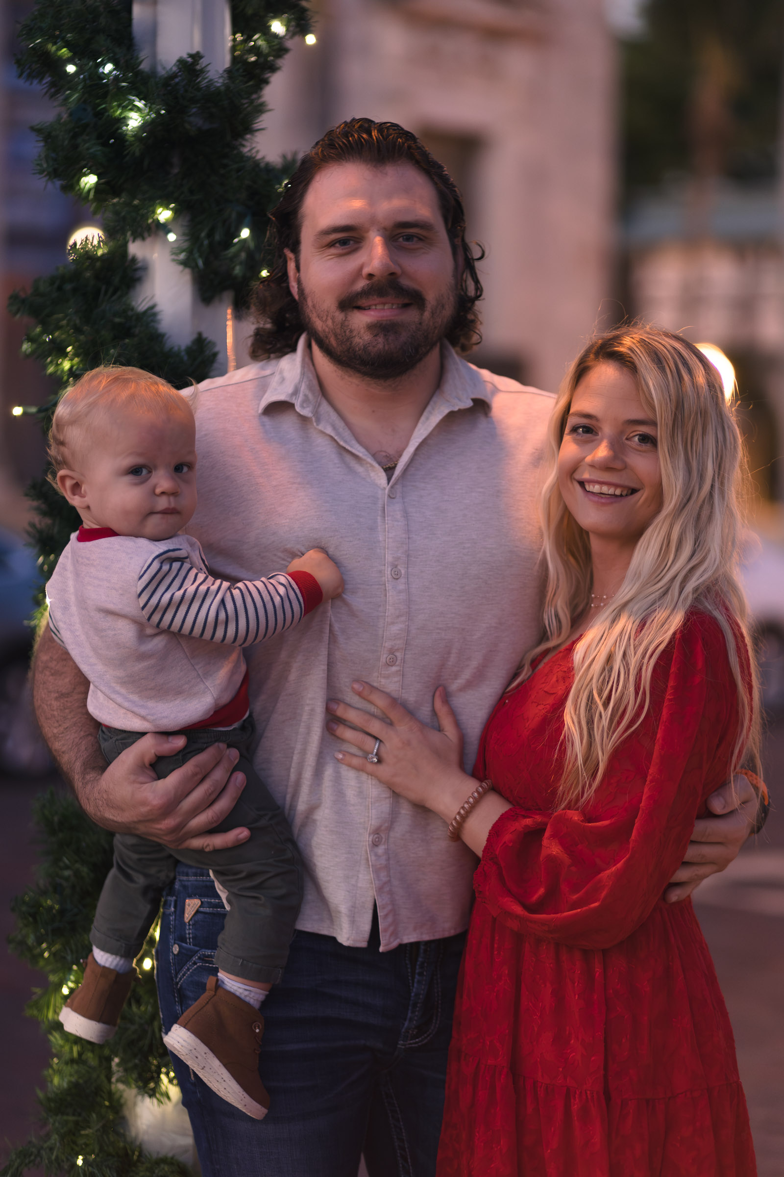 Family of 3 poses by a Christmas garland wrapped streetlight post in Fort Myers