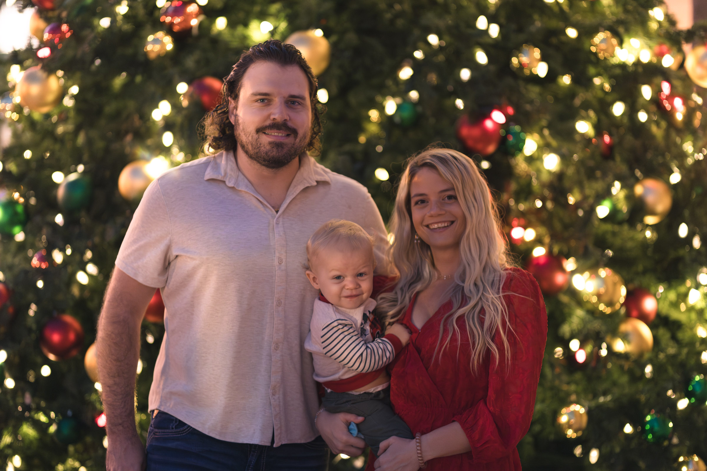 Family of 3 poses in front of a large Christmas tree in Fort Myers