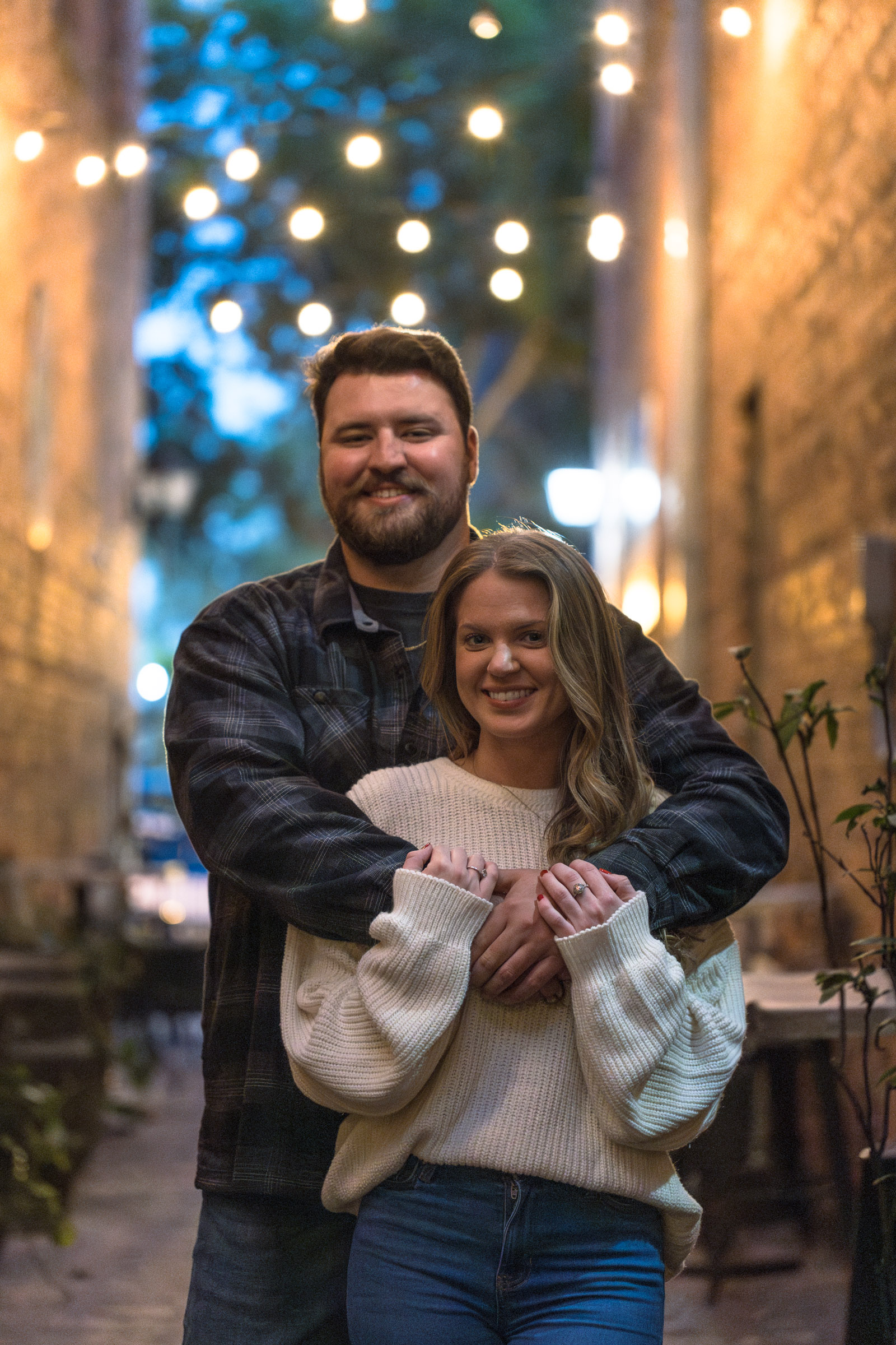 Man holds hugs his girlfriend with pretty lights in the background