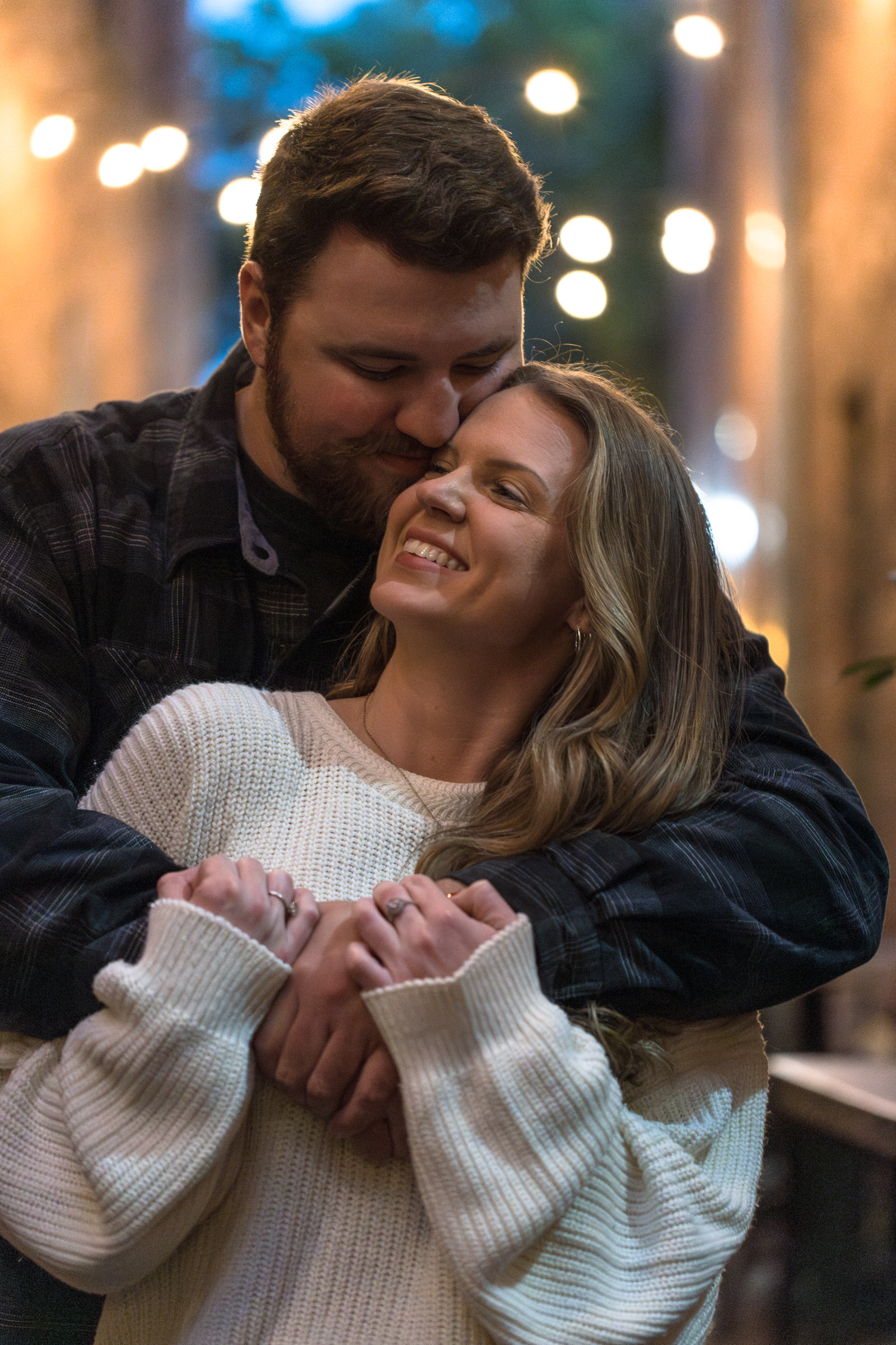 Man wraps his girlfriend in a hug with pretty lights in the background