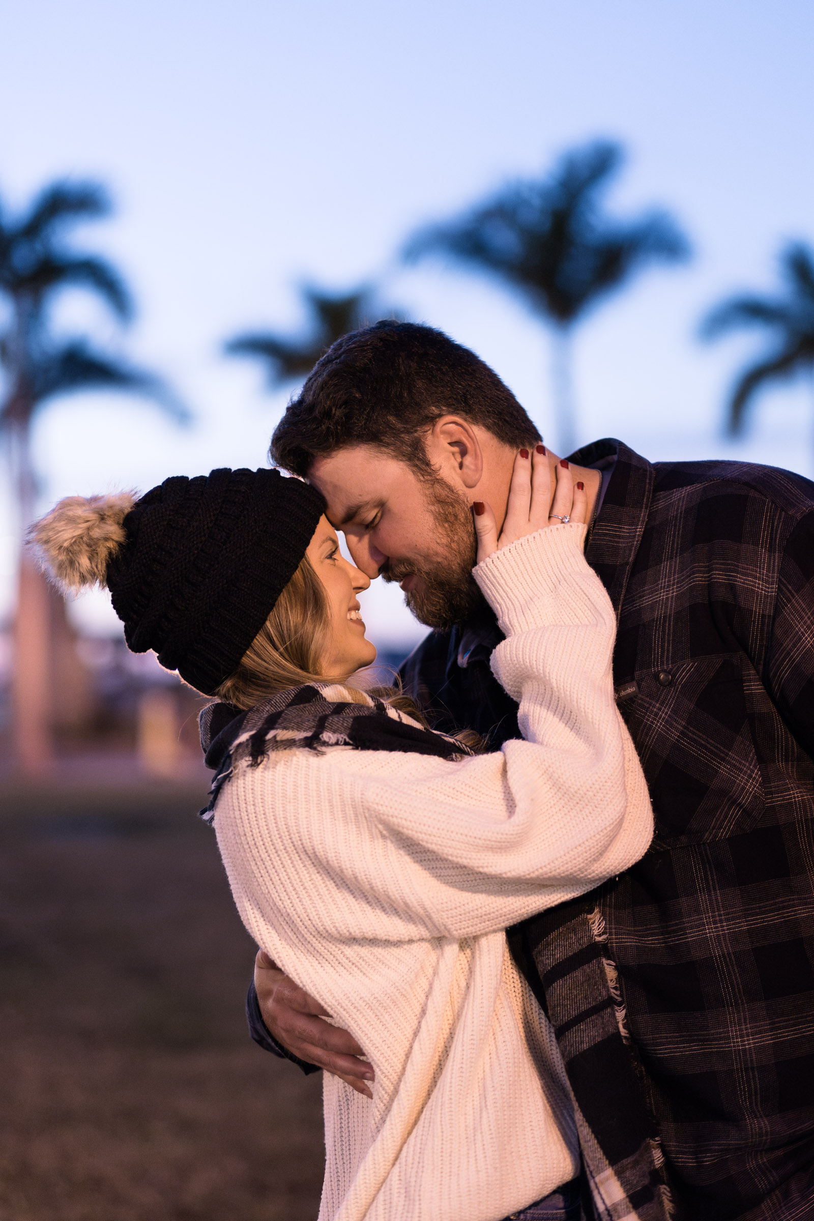 Couple dressed in winter clothes touching noses with blue hour skies in the background