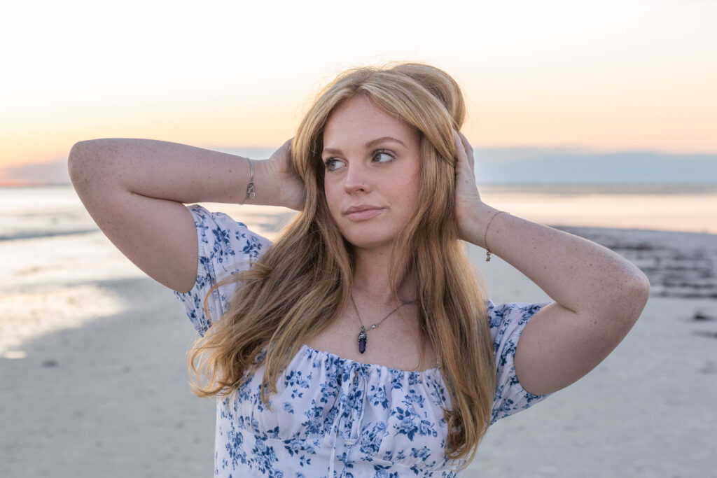 Young woman poses at the beach with her hands on her head