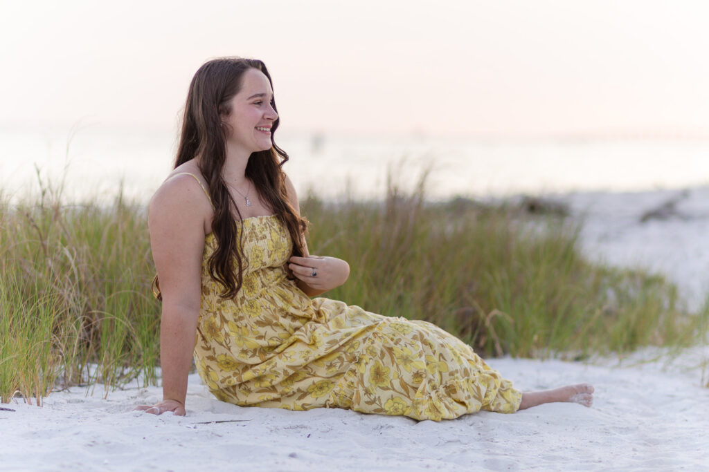 Woman in maxi dress sitting in beach in front of grass