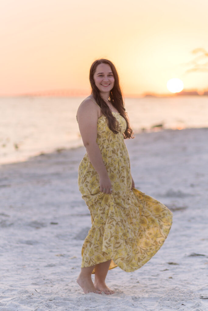 Woman twirls in maxi dress in front of orange beach sunset