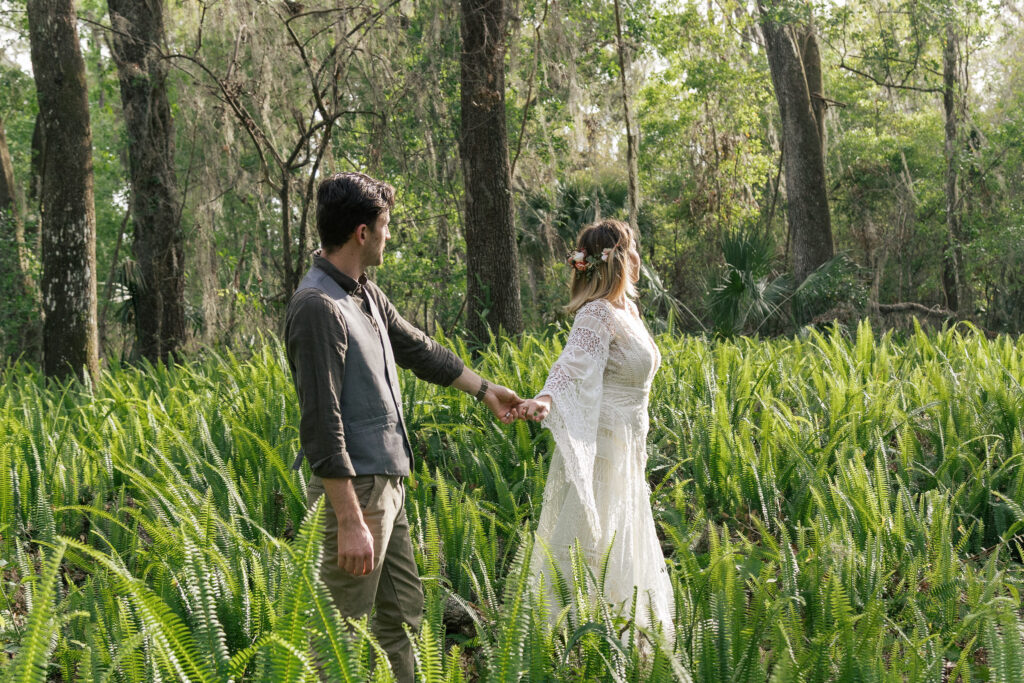 Bride leads her groom into a field of sunlit ferns