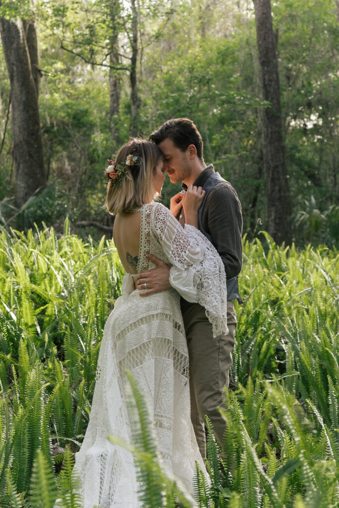 Couple peacefully rests foreheads together in a field of sunlit ferns