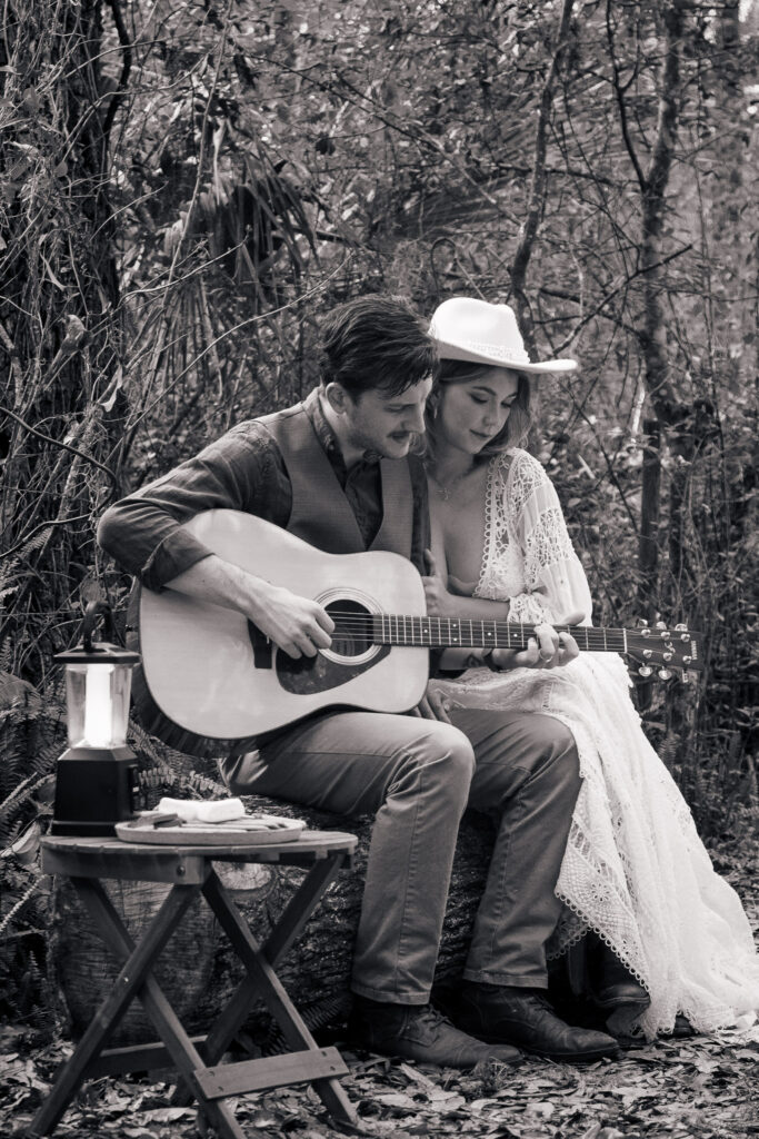 Black and white image of groom playing guitar next to his bride