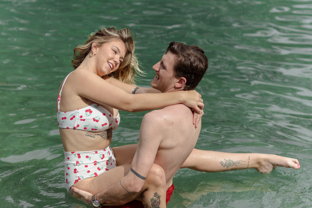 Man holds his wife in the water as she kicks her feet