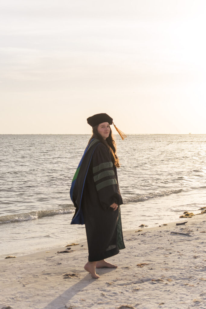 Woman walking away and smiling back, she's wearing graduation regalia