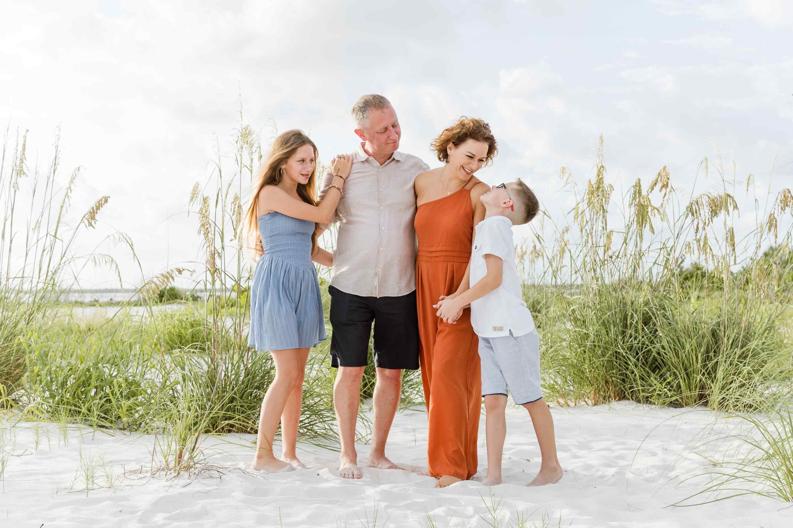 Family of four laughing together surrounded by beach grass