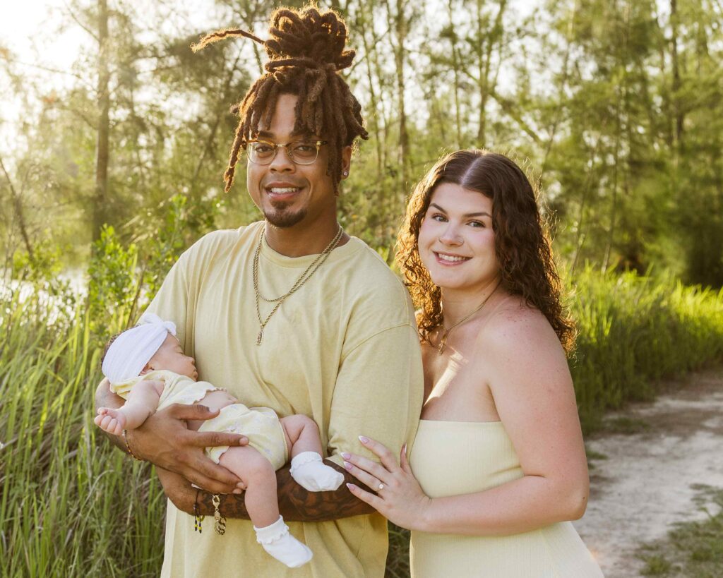 Family of three smile for a photo on a tree lined path