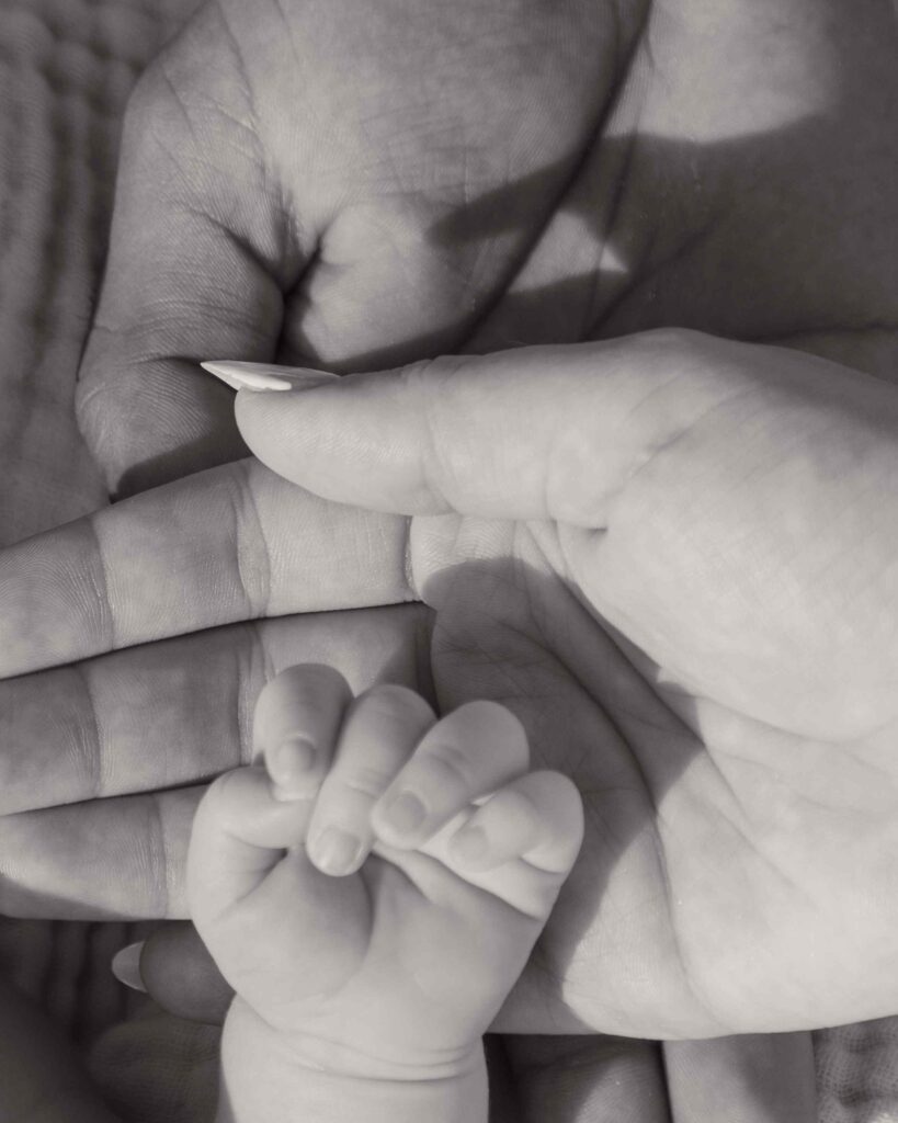 Greyscale closeup of family's hands stacked, dad, mom, and baby