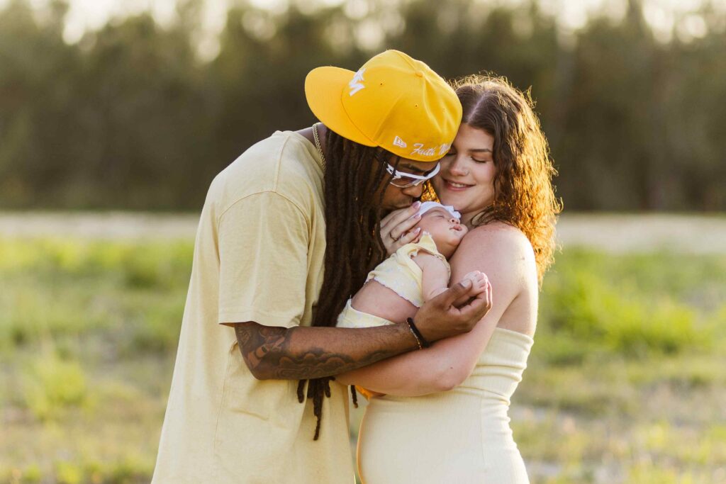 Family of three, dad kisses infant daughter on the head