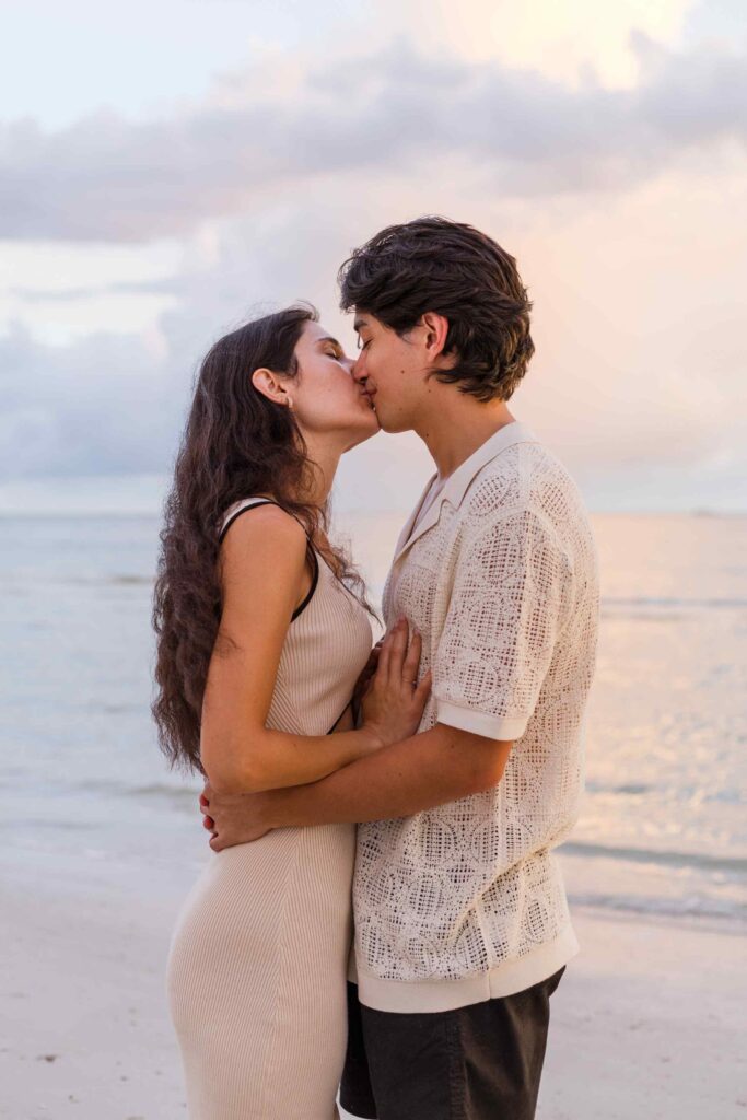 Couple kisses in front of a cotton candy colored sky