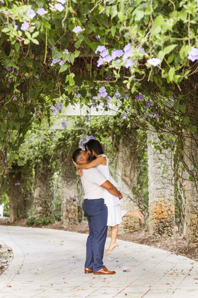 Man lifts up fiancée and kisses her in a flower tunnel
