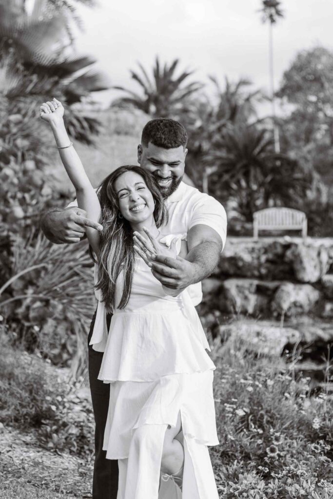 Black and white photo, woman and fiancé excitedly show off her new ring