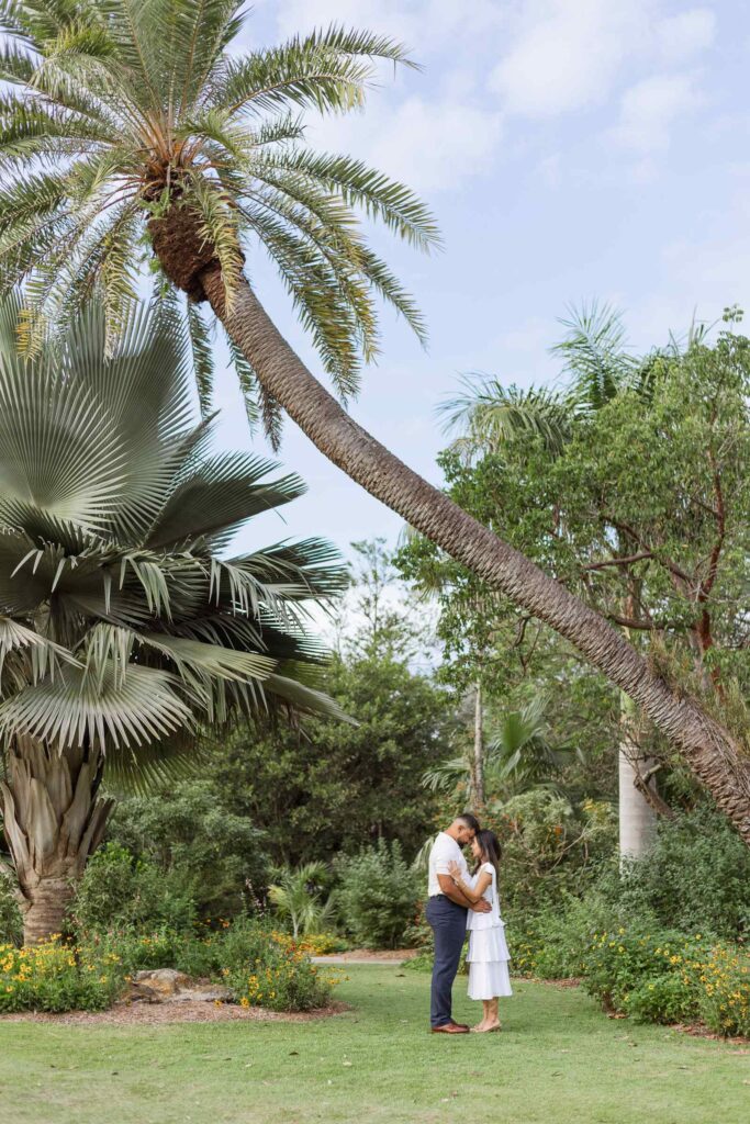 Couple forehead to forehead under a large palm tree at the Naples Botanical Garden