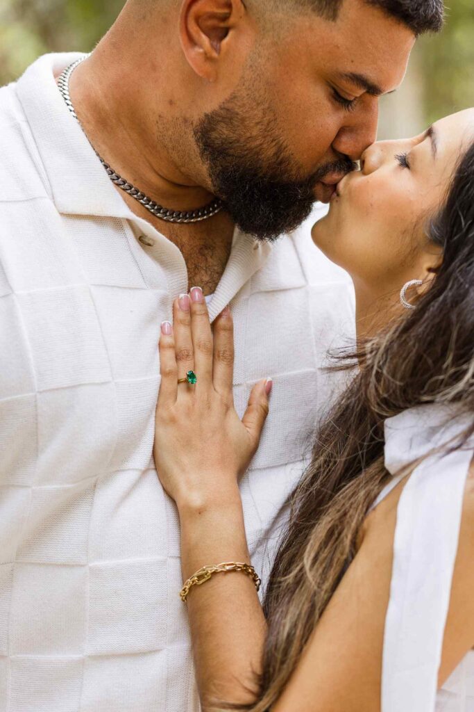 Photo of green engagement ring as couple kisses above
