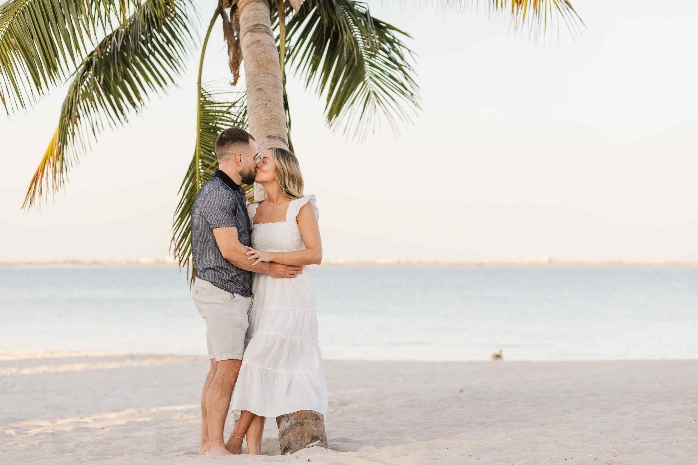 Couple kisses while leaning against a palm tree