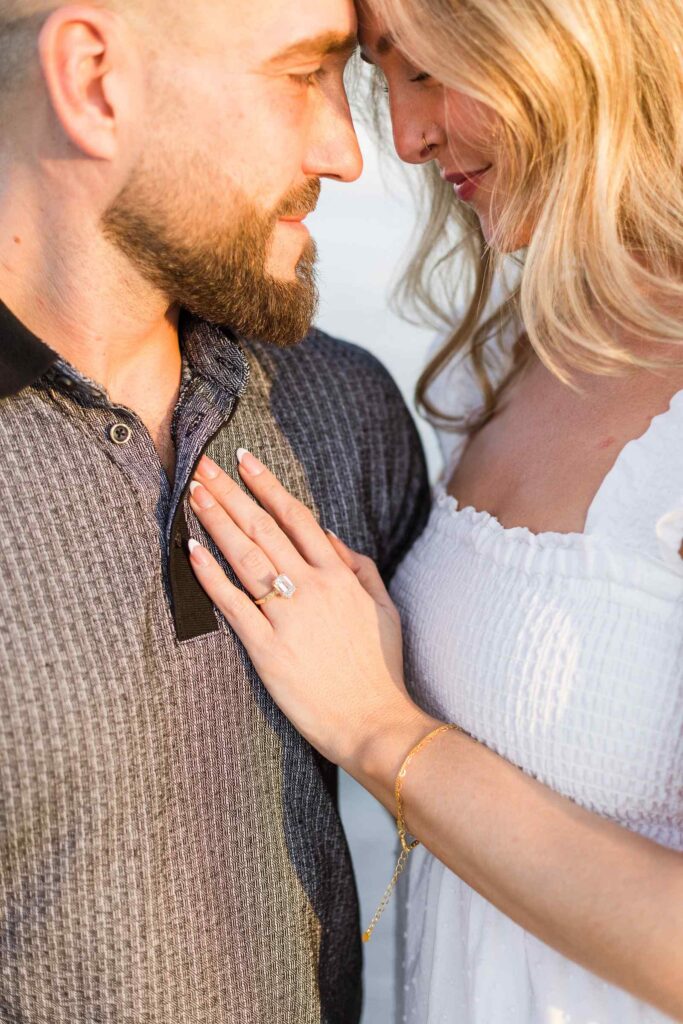 Image of couple forehead to forehead, the woman's hand is on the man's chest with her new engagement ring