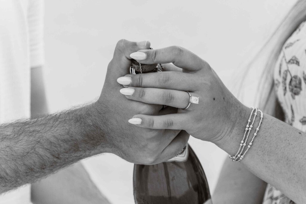 Couples hands on a bottle of champagne, they're celebrating after their marriage proposal