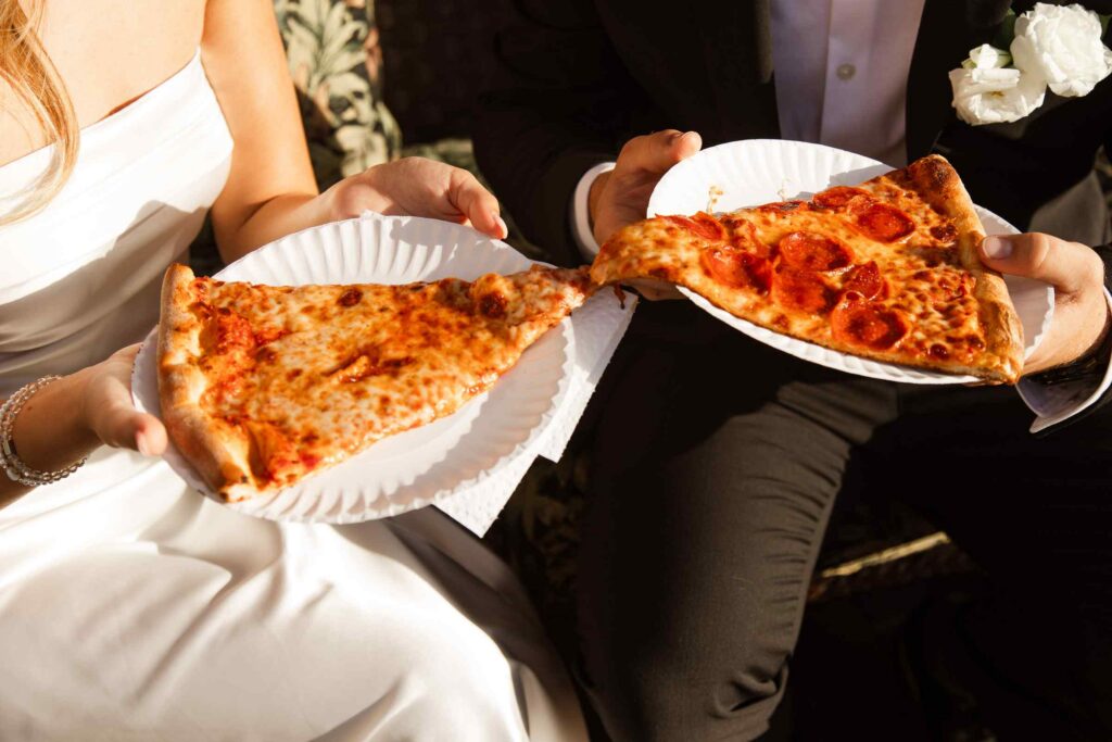 Close up of pizza slices held by bride and groom