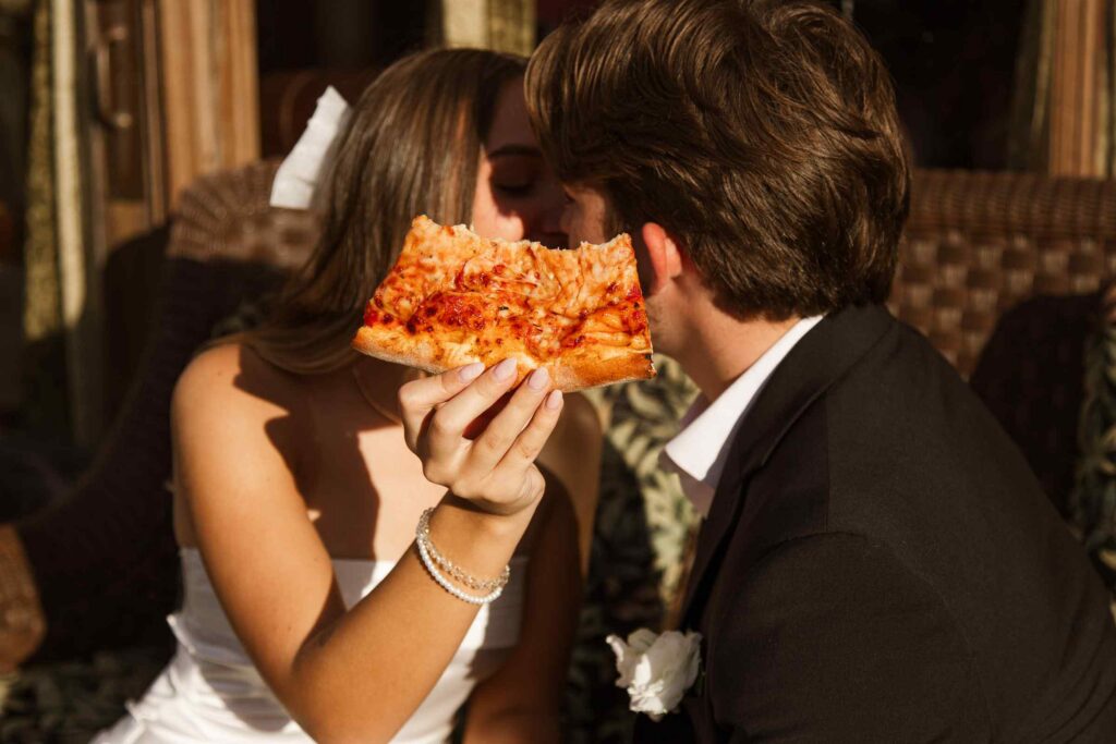 Bride and groom kiss behind a half eaten slice of pizza