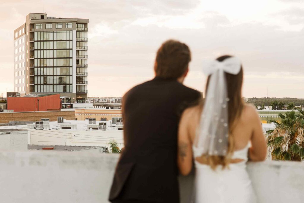 Bride and groom look out from a parking garage in Downtown Fort Myers, camera is focused on the Luminary in the background