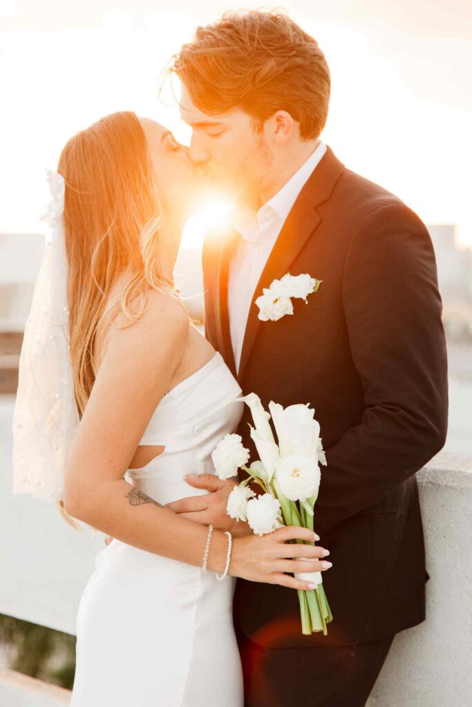 Bride and groom kiss with a golden hour flare in between them
