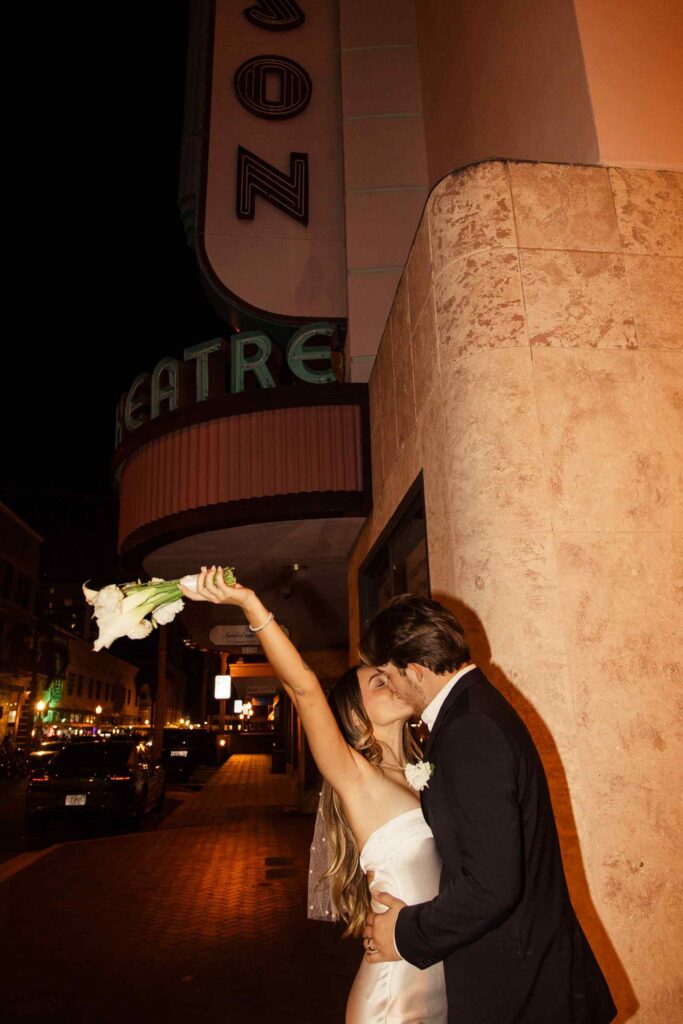 Bride holds bouquet up celebrating in front of the Edison Theatre