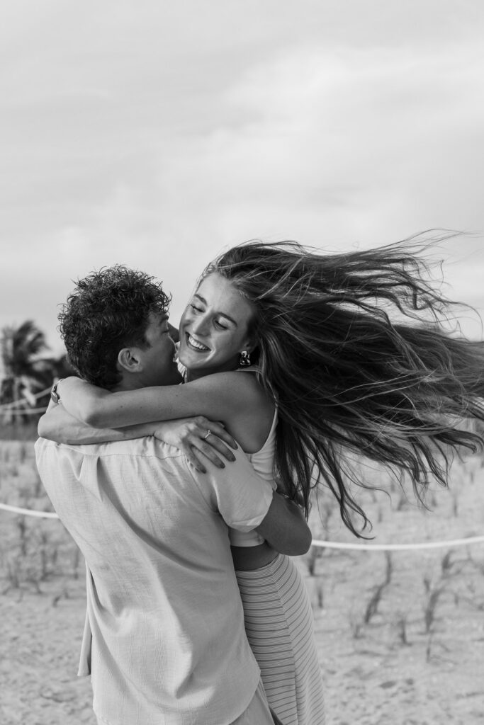 Black and white image, man picks up fiancée and spins her around with her long hair flying out to the side