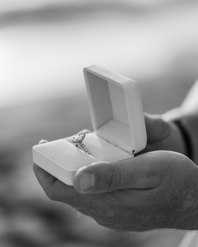 Black and white image, close up of man holding engagement ring in a white ring box