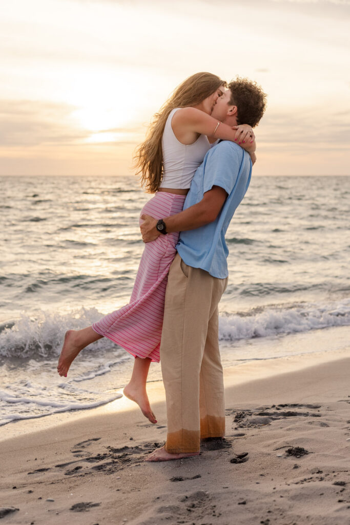 Man lifts fiancee up for a kiss on the beach