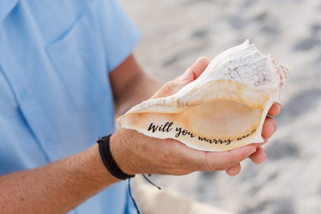 Man holds shell that says "will you marry me?" inside