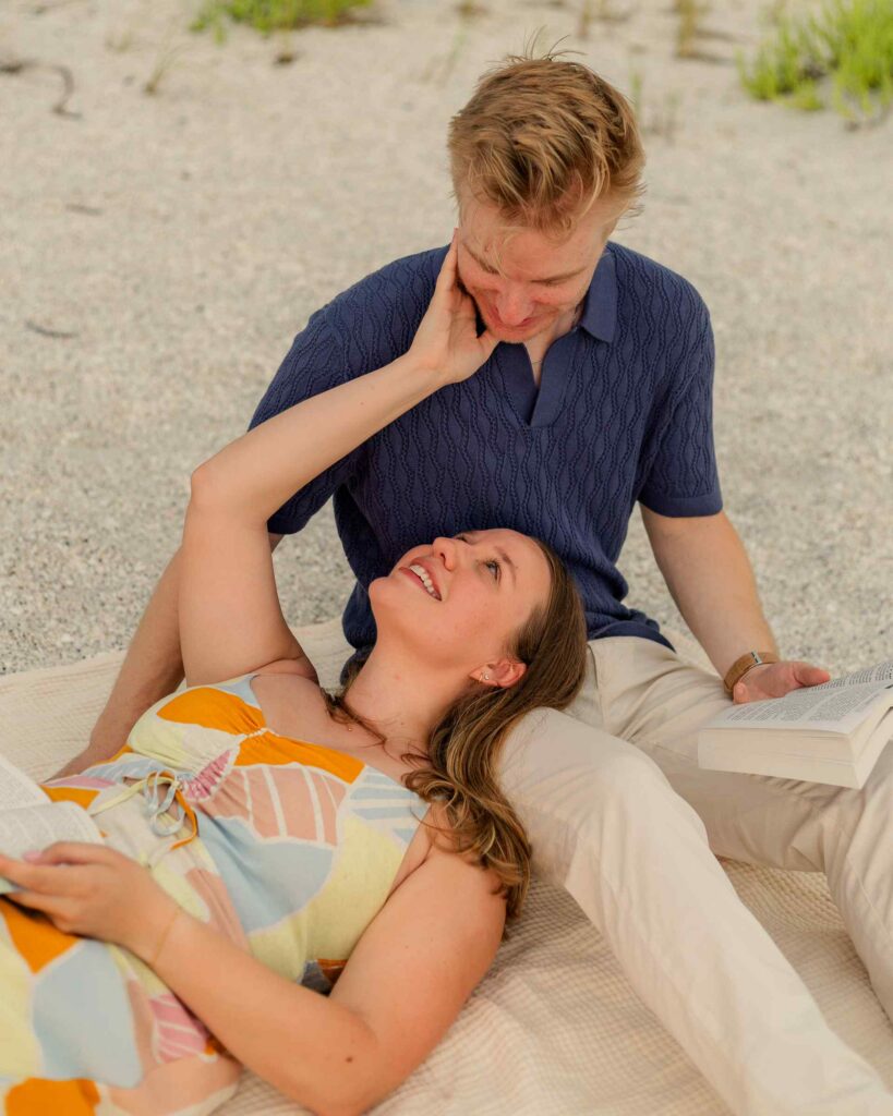 Woman lies with her head in her fiance's lap reading and smiling up at him