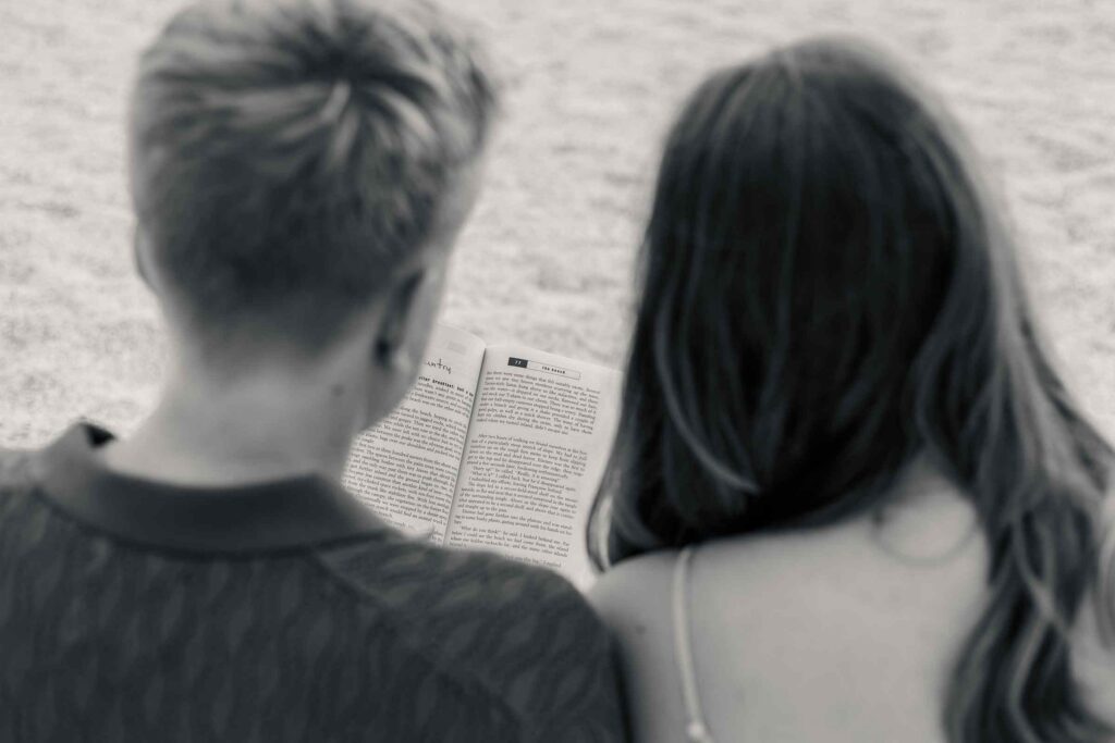 Black and white image over couple's shoulders with the book they're reading in the background