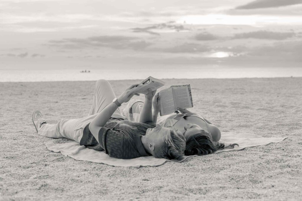 Black and white image of couple laying on the beach reading together