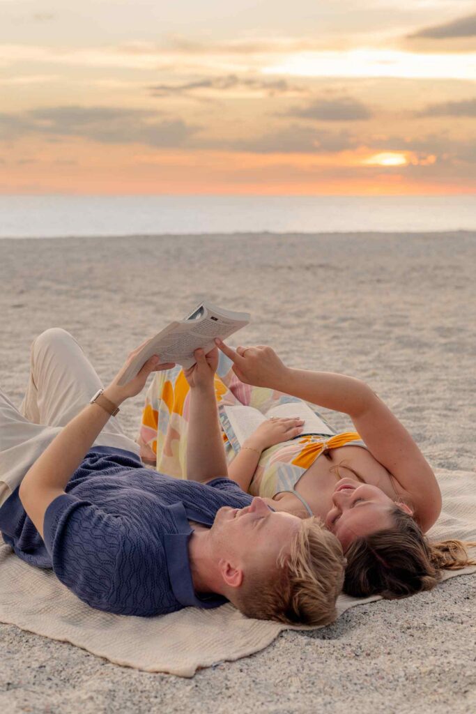Couple reading together on the beach at sunset, the woman is pointing to a line in the book