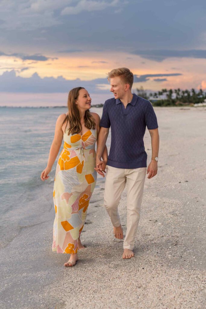 Couple walking on the beach with a blue and orange sunset behind them